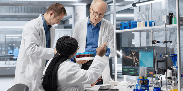 Three scientists in lab coats working together in a modern laboratory setting