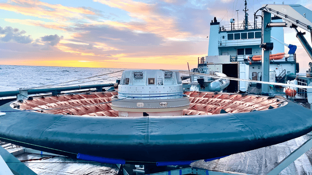 A research vessel deck with a circular device against a colorful sunset sky