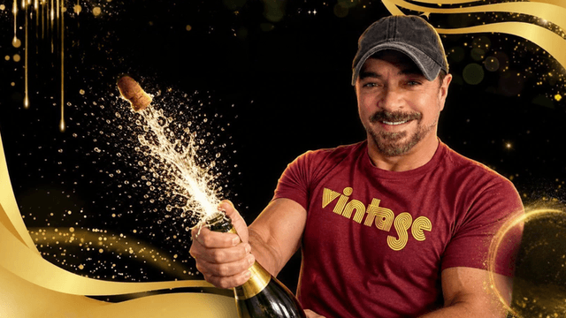 Smiling man in a cap opening champagne with sparkling bubbles around him
