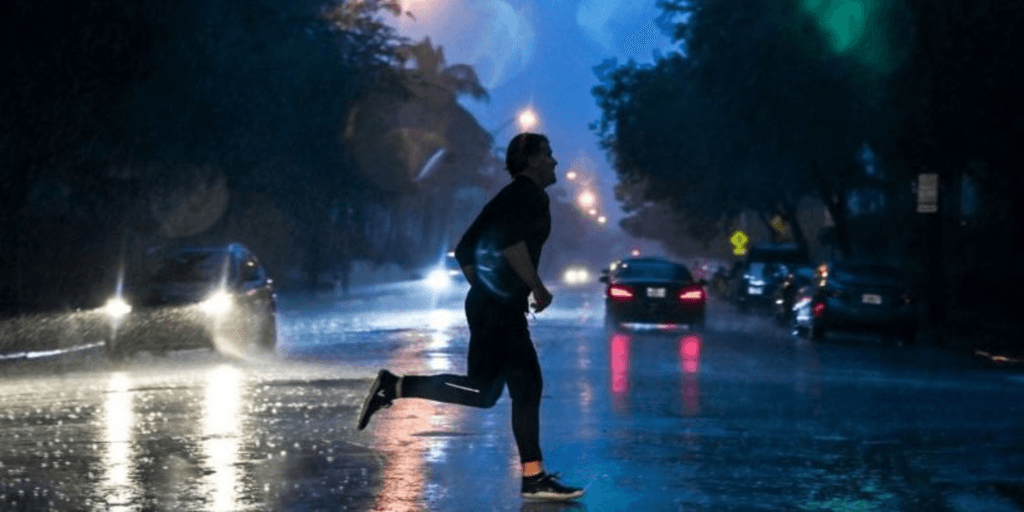 Person running in heavy rain on a dimly lit street with cars passing