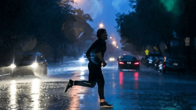 Person running in heavy rain on a dimly lit street with cars passing