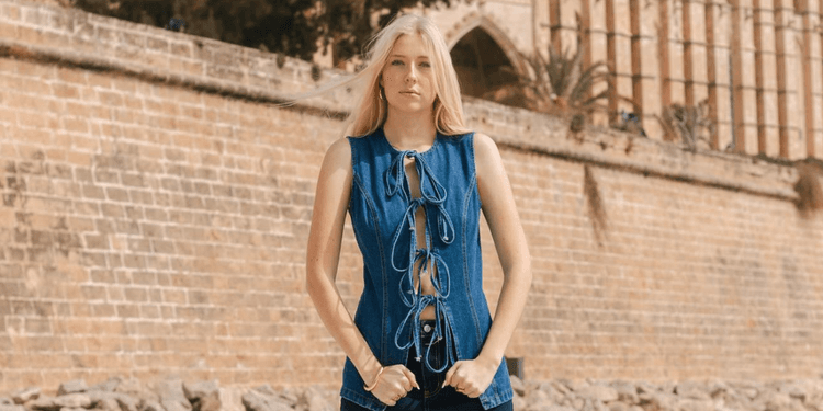 Emilia Knudsen wearing a blue lace-up denim top in front of a historic stone building.