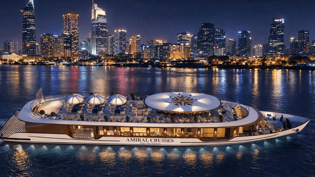 Luxury river cruise yacht illuminated at night on Saigon River with Ho Chi Minh City skyline.
