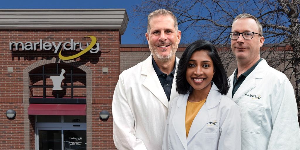 Three pharmacists in lab coats stand outside Marley Drug's building, offering affordable medication solutions with transparent pricing model.
