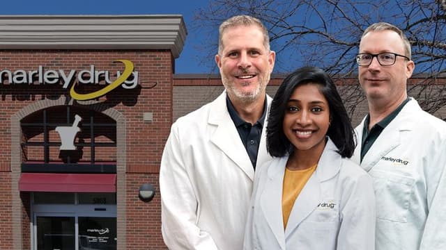 Three pharmacists in lab coats stand outside Marley Drug's building, offering affordable medication solutions with transparent pricing model.
