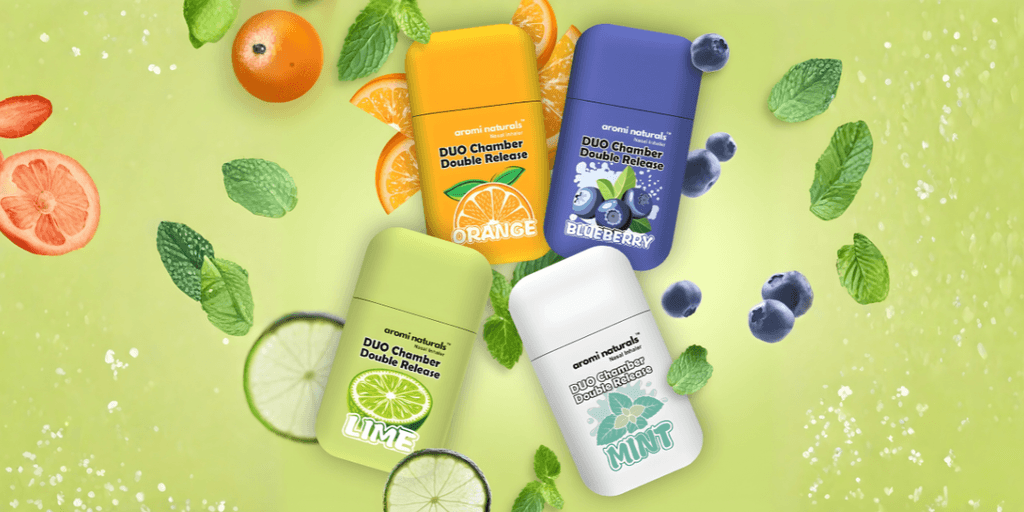 Four Aromi Naturals inhalers in fruity flavors: Orange, Lime, Blueberry, and Mint, surrounded by mint leaves and citrus slices.