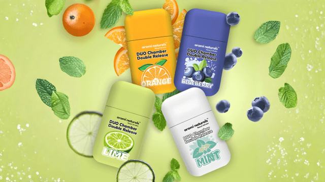 Four Aromi Naturals inhalers in fruity flavors: Orange, Lime, Blueberry, and Mint, surrounded by mint leaves and citrus slices.