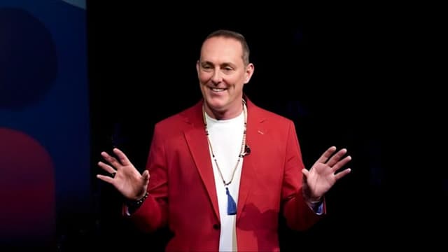 TJ Woodward, in a red blazer, delivering a speech, embodying his Conscious Creation Model to empower intentional living.
