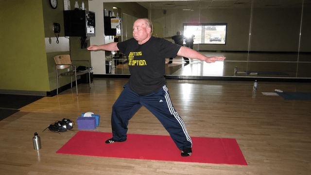 Person practicing a yoga pose on a red mat in a fitness studio.
