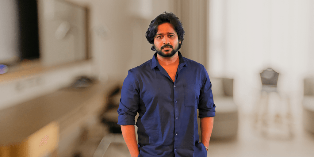 Man in navy shirt standing indoors with blurred background, portrait-style professional image.