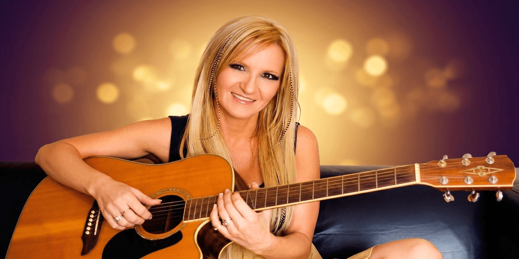 Woman smiling while holding an acoustic guitar against a glowing background.