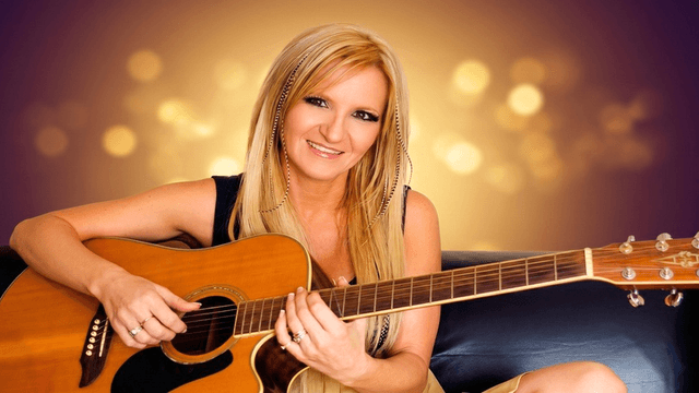 Woman smiling while holding an acoustic guitar against a glowing background.
