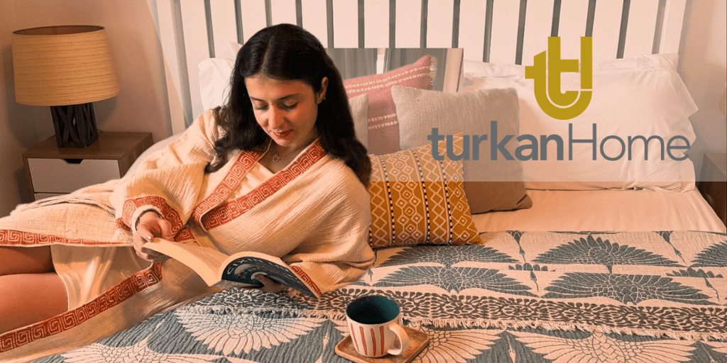 A cozy bedroom featuring TurkanHome textiles, including a decorative blanket, cushions, and a woman reading, embracing mindful living.