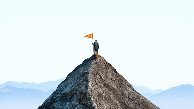 A person in a suit stands on a mountain peak, holding an orange flag, symbolizing personal transformation and success