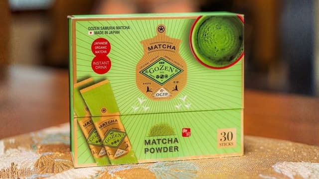 Gozen matcha powder box with individual sticks and a bowl of bright green matcha.