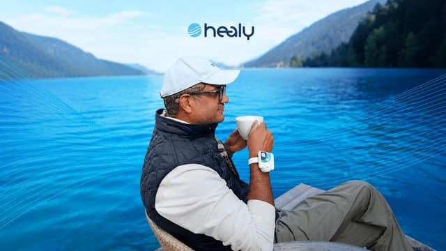 Person wearing a Healy device while enjoying a lakeside view with a cup of coffee.