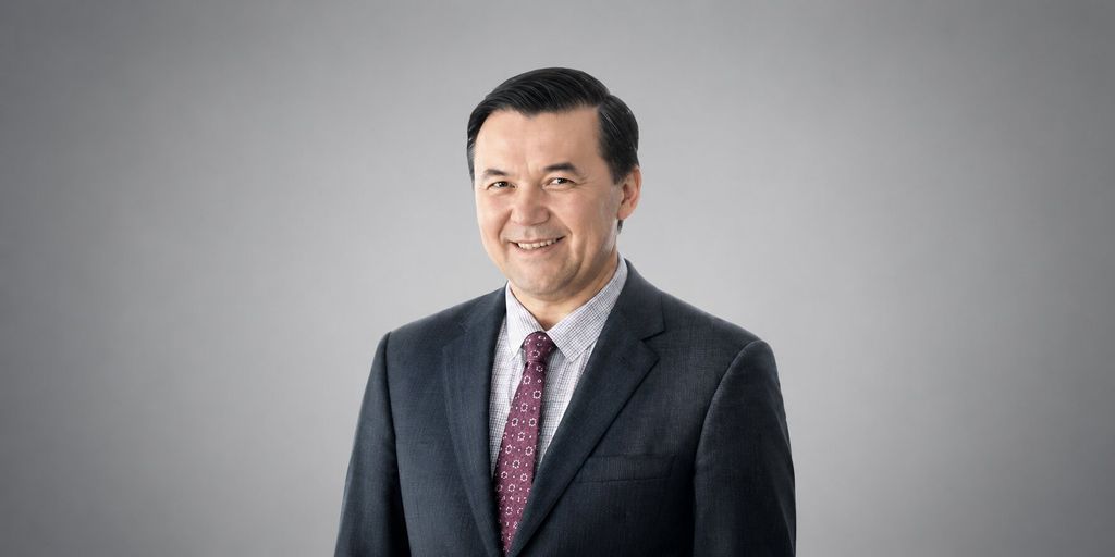 Smiling businessman in dark suit and patterned tie against gray studio background.