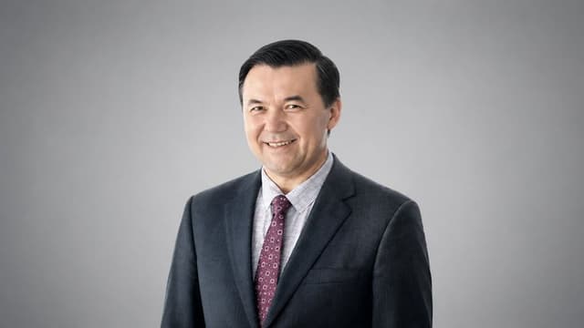 Smiling businessman in dark suit and patterned tie against gray studio background.