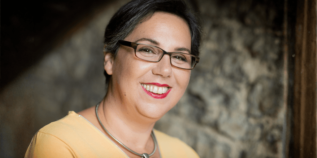 Einav Avni, a healing coach, smiling warmly while wearing glasses and a yellow top, exuding calm and confidence.