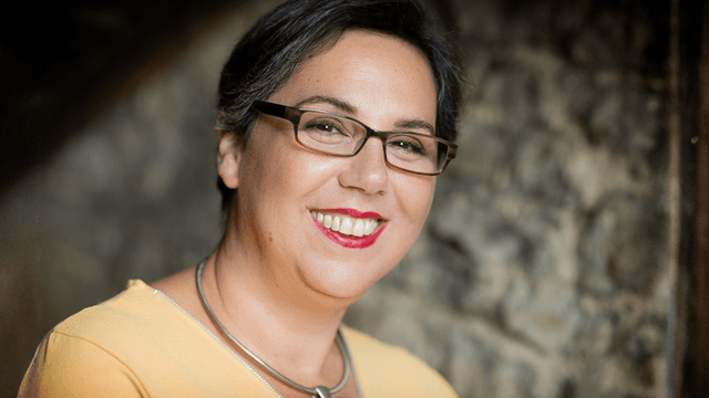 Einav Avni, a healing coach, smiling warmly while wearing glasses and a yellow top, exuding calm and confidence.