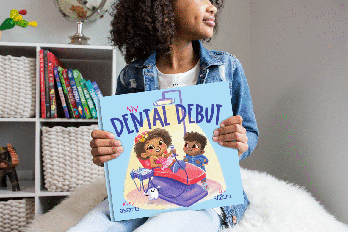 A child holds the book My Dental Debut, featuring two animated characters at a dental appointment.