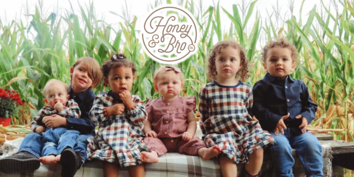 Six children dressed in cozy, eco-friendly outfits from Honey and Bro Co., seated together with a cornfield backdrop.