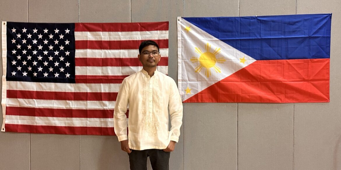 Ranell Engay stands proudly between the American and Philippine flags, symbolizing his global impact in science education.