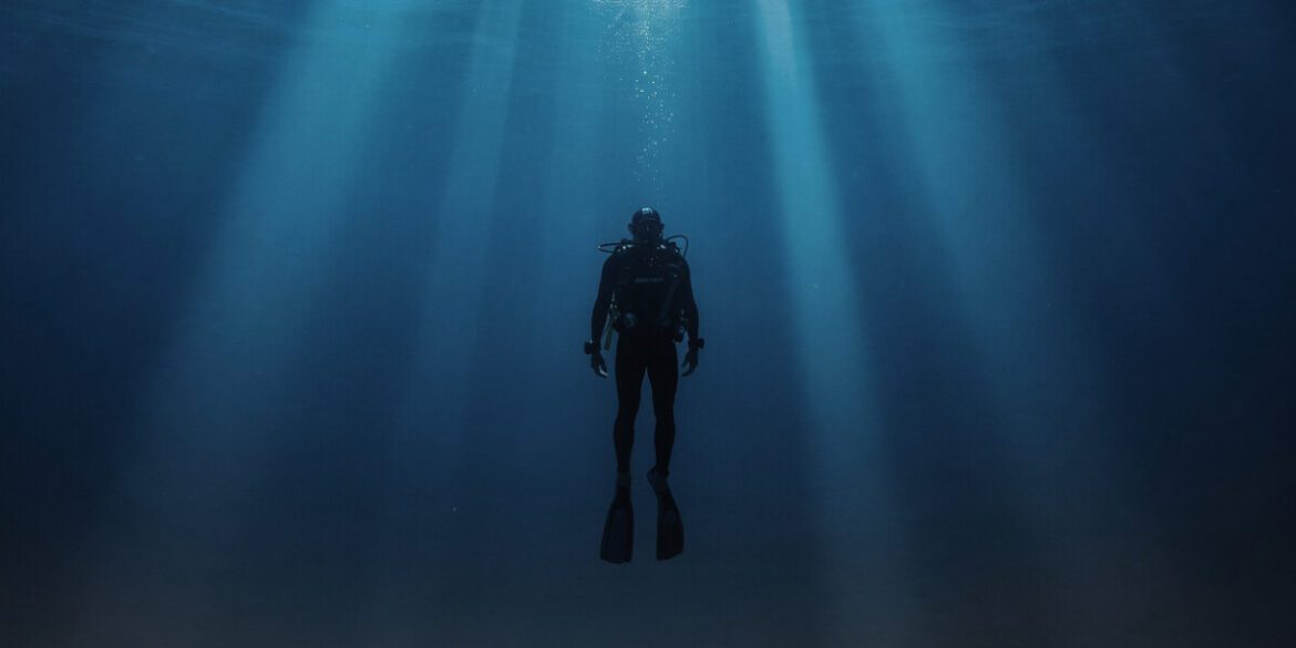 A diver immersed in the calm, deep blue of the ocean, illuminated by rays of sunlight filtering through the water.