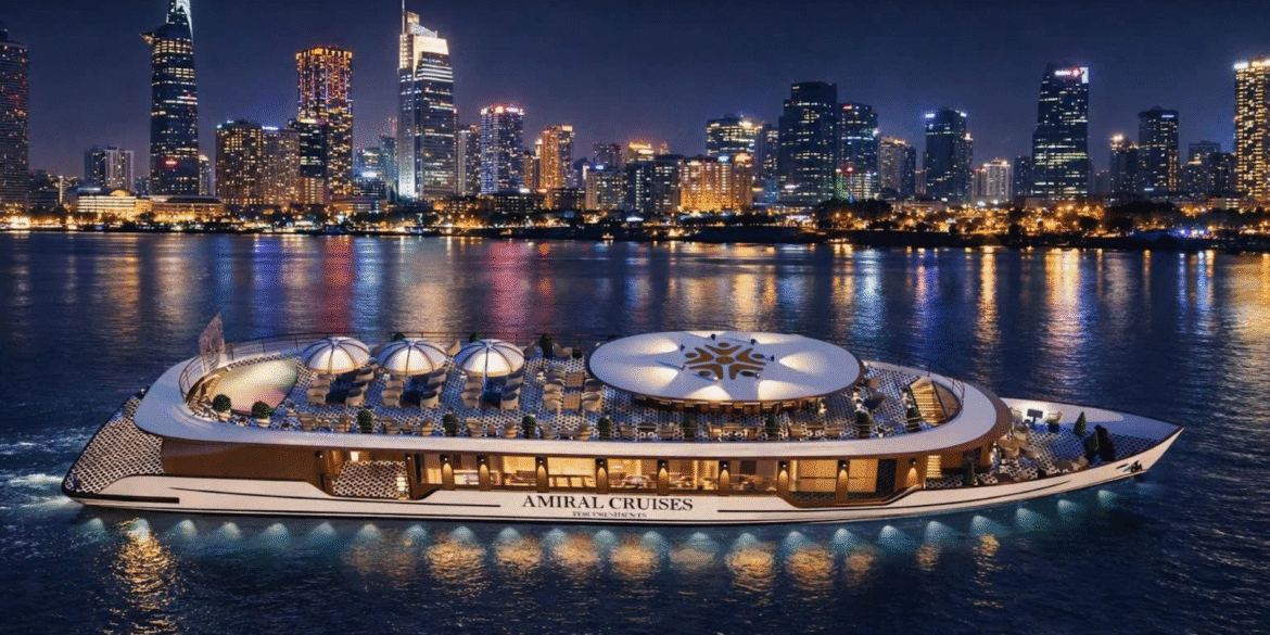 Luxury river cruise yacht illuminated at night on Saigon River with Ho Chi Minh City skyline.