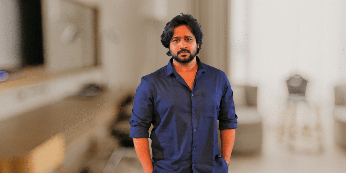 Man in navy shirt standing indoors with blurred background, portrait-style professional image.