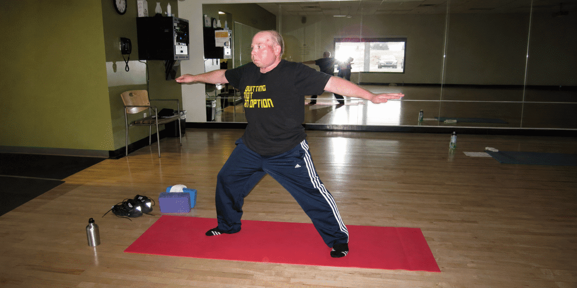 Person practicing a yoga pose on a red mat in a fitness studio.