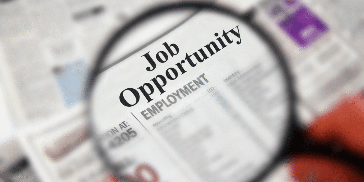 Magnifying glass enlarges the words “Job Opportunity” and “Employment” on a printed jobs page.