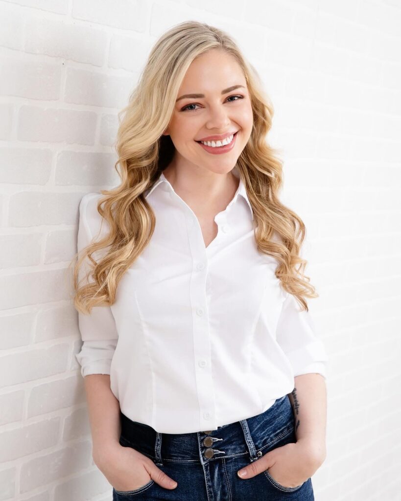 Kellsey Forest smiling in a white blouse against a white brick wall.