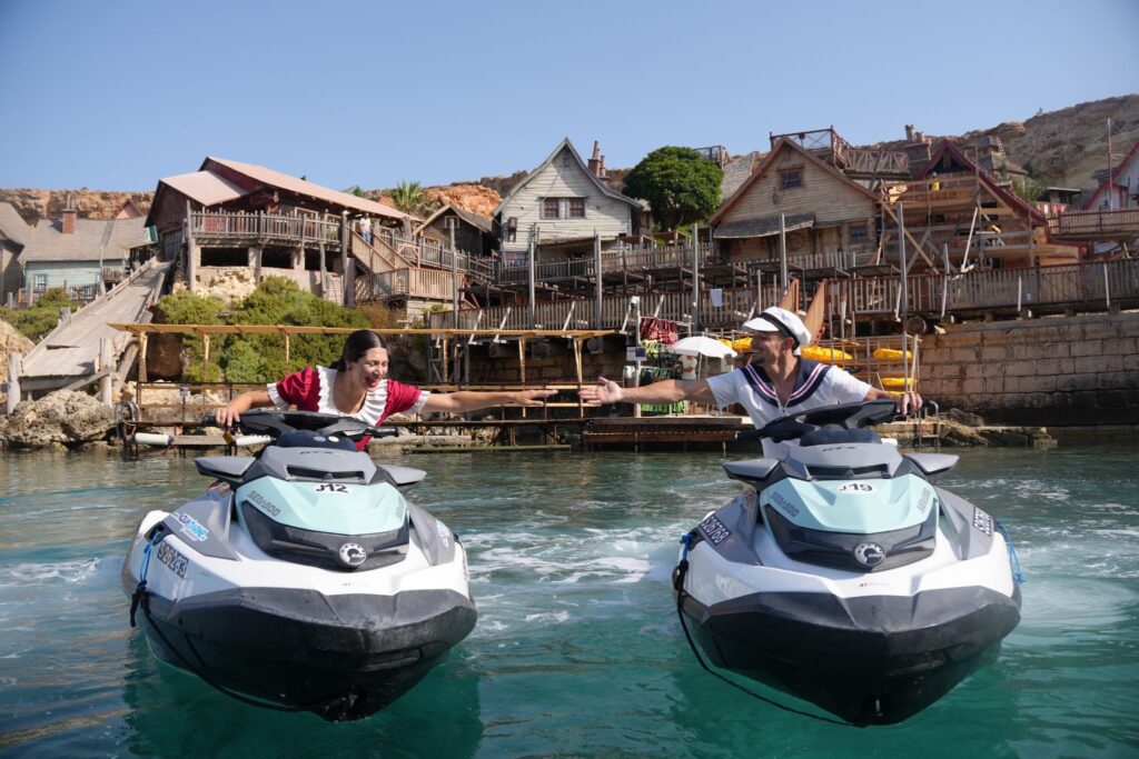 Two people on Sea-Doo jet skis reaching toward each other on the water beside Popeye Village.